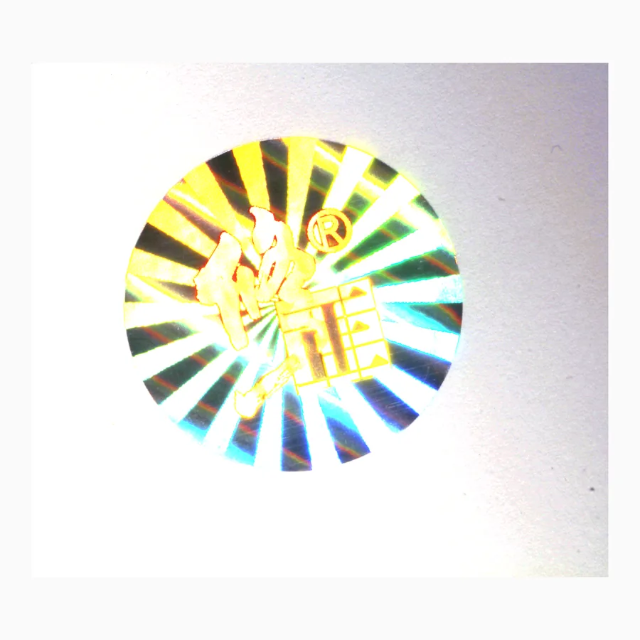 Circular holographic security label showing a radial diffraction pattern shifting through green and gold
